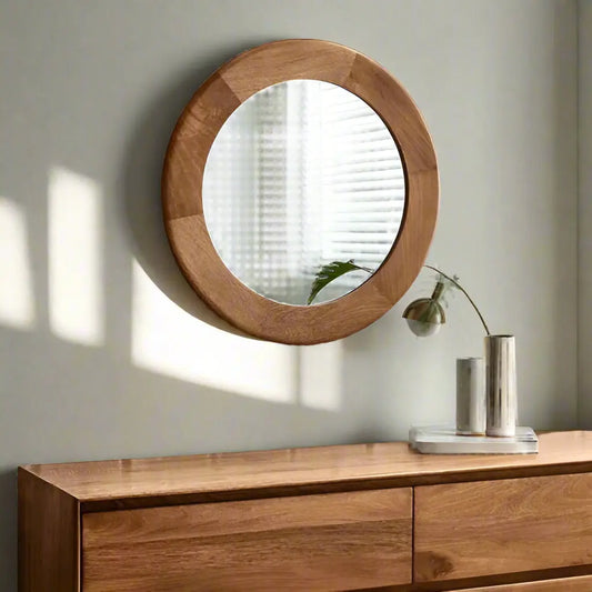 A round mirror with a wooden frame, hanging on a wall above a wooden dresser.