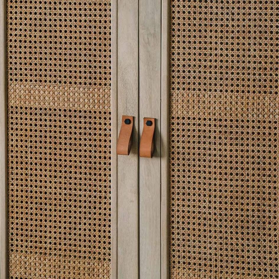 Close-up of a cabinet door with woven cane or rattan panels and two small rectangular leatharite handles.