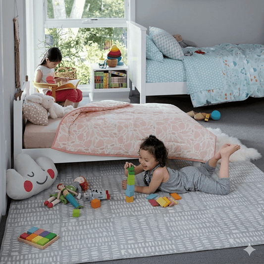 A child playing with toys on the floor next to a small, brown wooden bed with a child sitting on it in a bedroom setting.