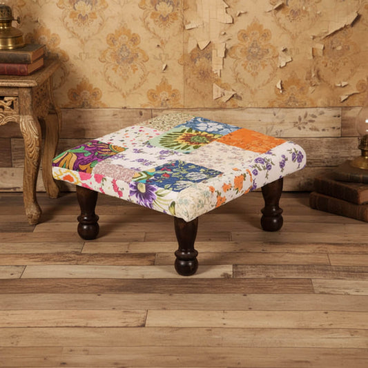 A square-shaped Patchwork Chowki with multicolored floral and geometric patterned fabric on top, supported by four wooden legs.