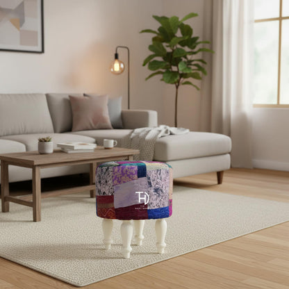 A multicolored patchwork pouf with silk upholstery on a Sheesham wood structure, with white-painted legs.
