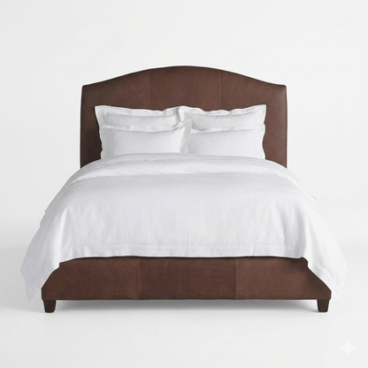 A bed with a brown headboard and white bedding, with a decorative white blanket on the bed.