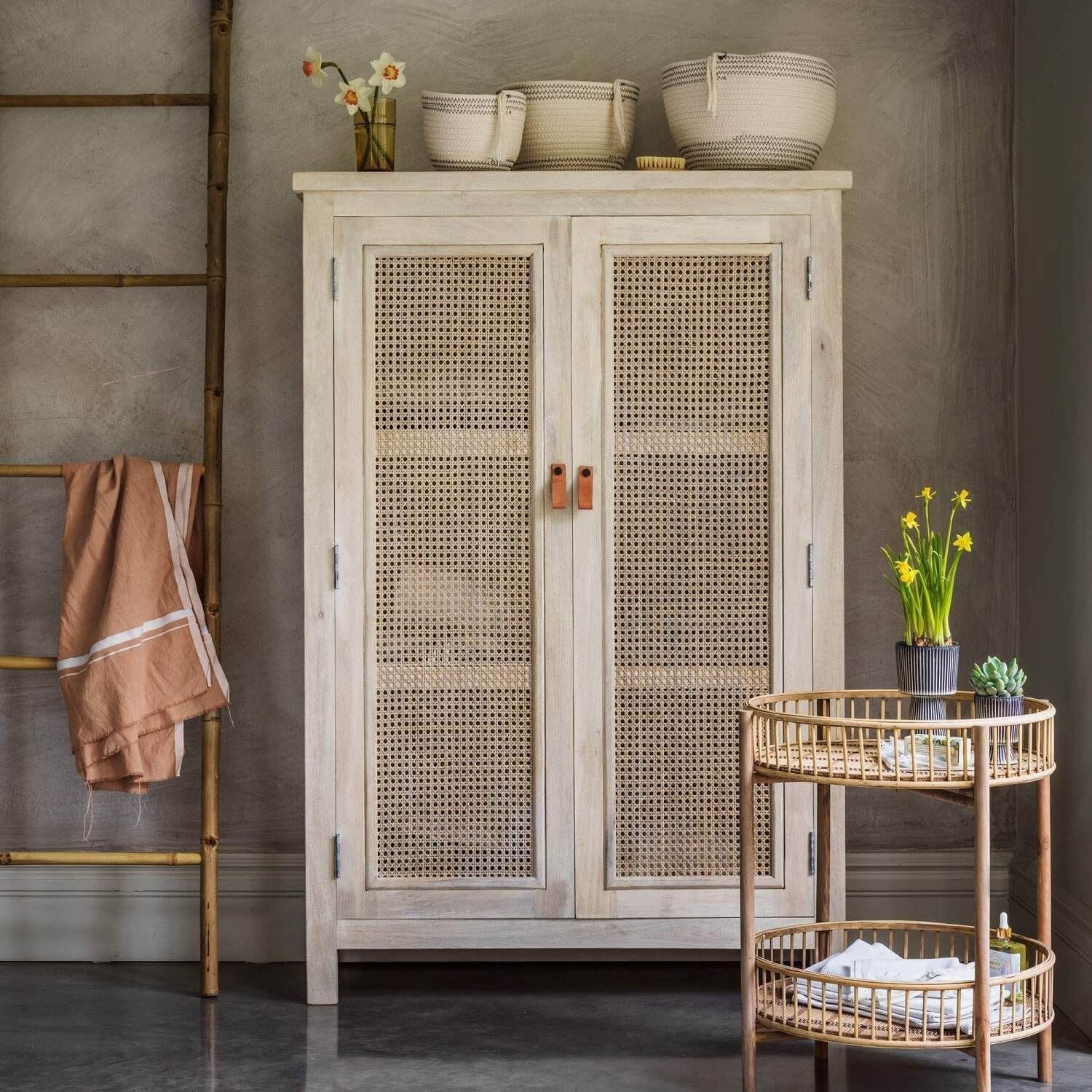 A white wash finish cane almira with two doors, placed in a room with various decor items around it.