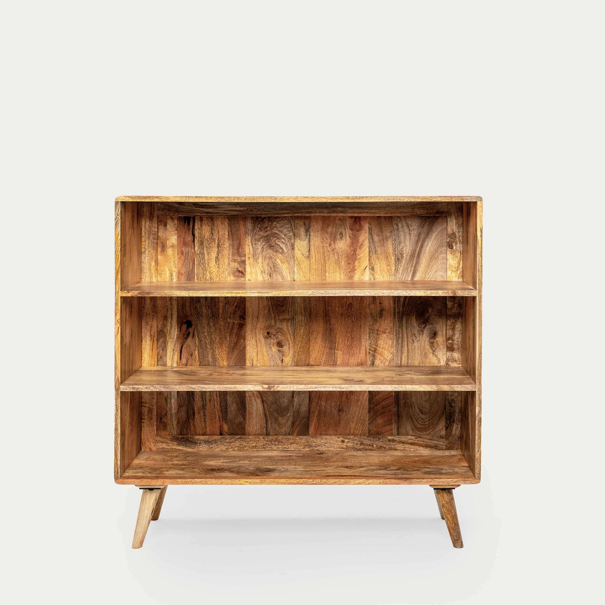 A rustic mango wood bookcase with three shelves and tapered legs.
