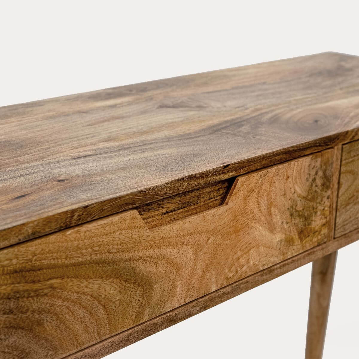 Close-up of a wooden writing desk or console table showing the grain of the wood on the desktop, drawer front, and leg.