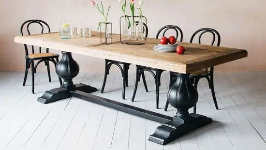 A sturdy mango wood dining table with solid turned legs, featuring a natural wood finish and a black metal base.