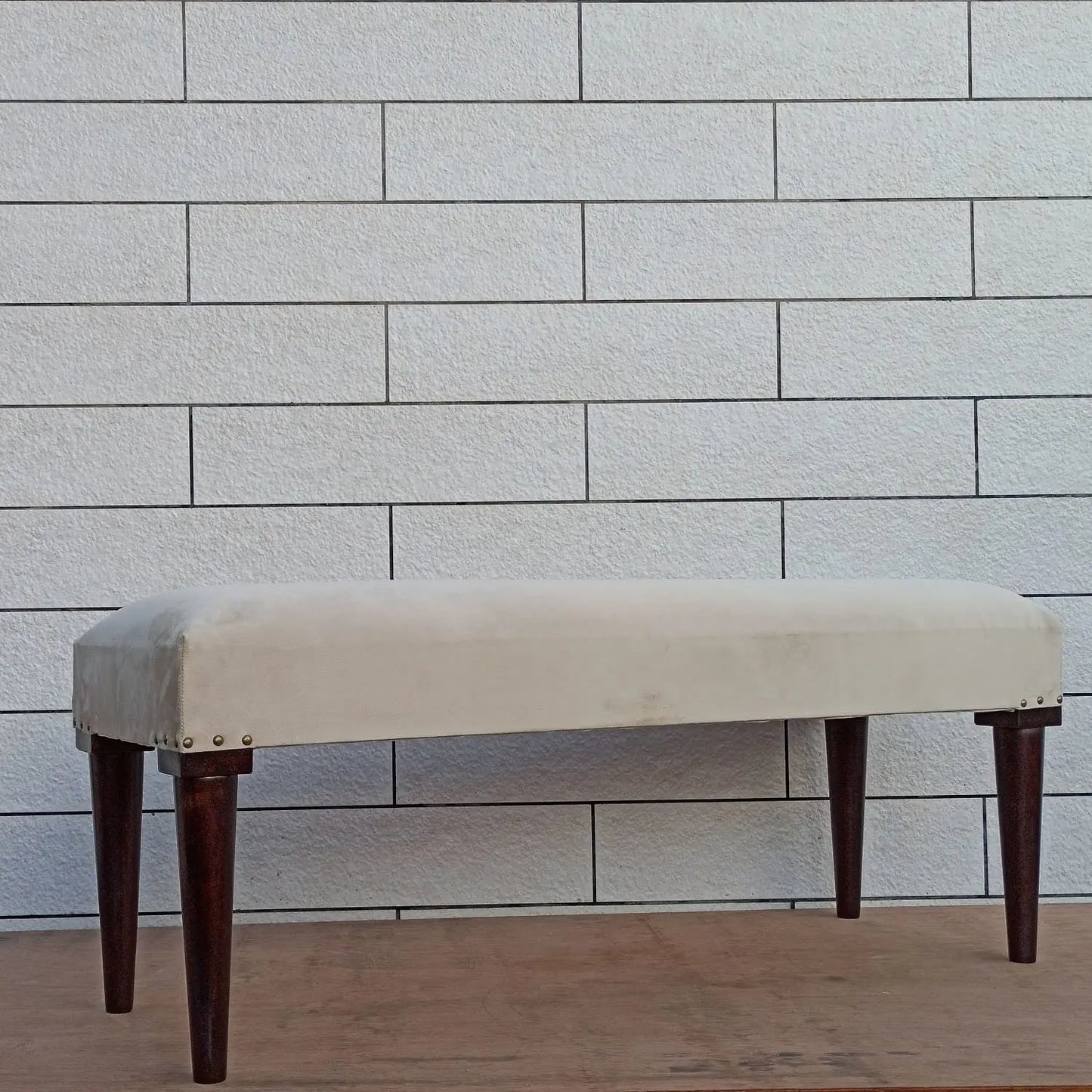 Beige upholstered carvin bench with dark round wooden legs.