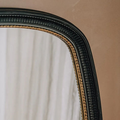 Close-up of a decorative wall mirror with a dark black frame featuring a raised beaded gold inner border.