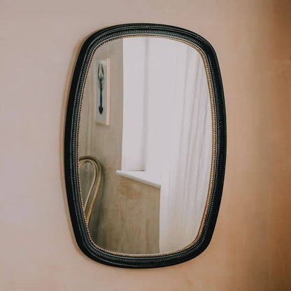 An oval wall mirror with a textured black frame and a gold inner trim.