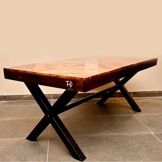 A rectangular dining table with a herringbone design top made of sheesham wood and X-shaped metal legs.