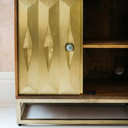 The shutter has a tactile feature that adds a third dimension to the cabinet. The unit has a patina finish with traditional knobs with carving details.