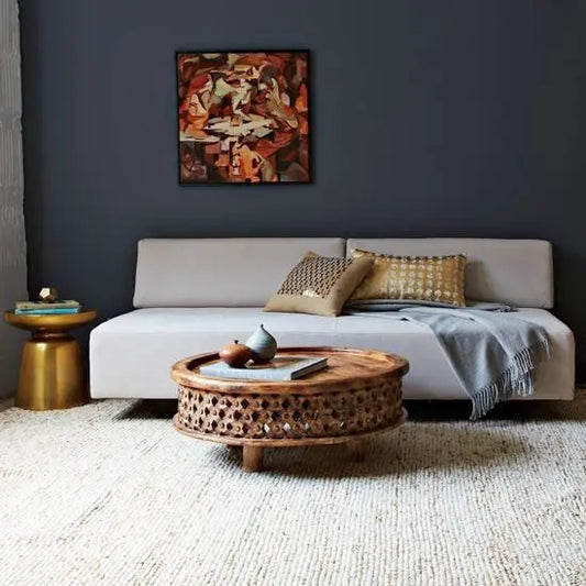 A hand-carved, round, mango wood coffee table with intricate patterns.