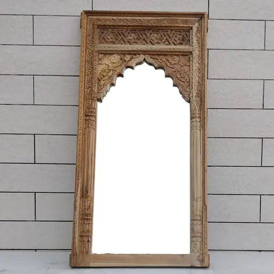 An ornate wooden mirror frame with carved design in top side finish in teak natural.