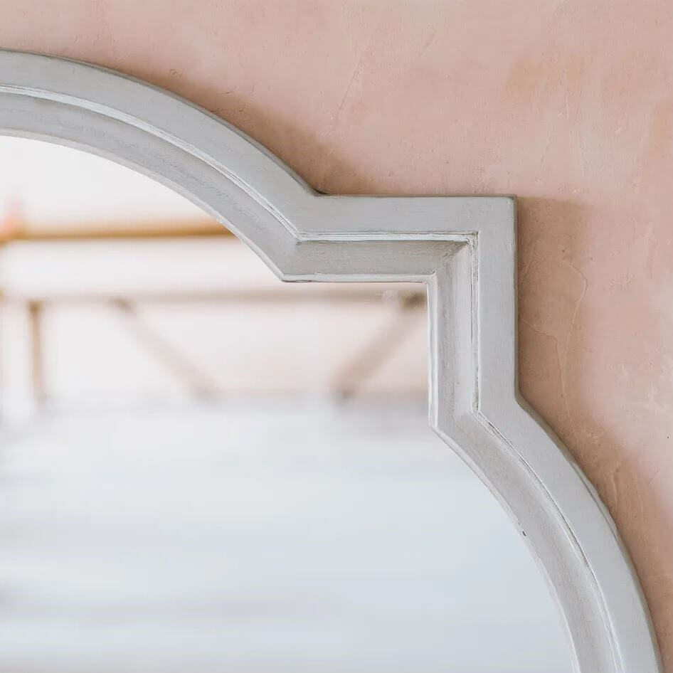 A close-up of a decorative wall mirror with a distressed white frame.