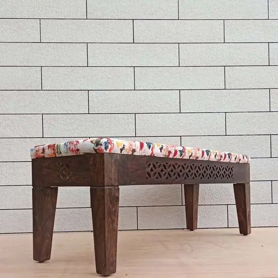 A wooden bench with dark finish and carved details on sides.