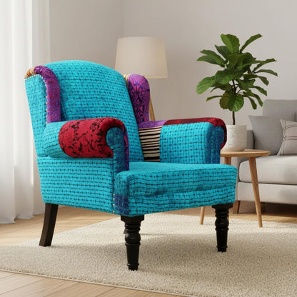 A blue Maharaja sofa with velvet upholstery and wooden legs, featuring a single seat and patchwork on the armrest.