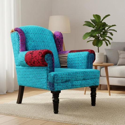 A blue Maharaja sofa with velvet upholstery and wooden legs, featuring a single seat and patchwork on the armrest.