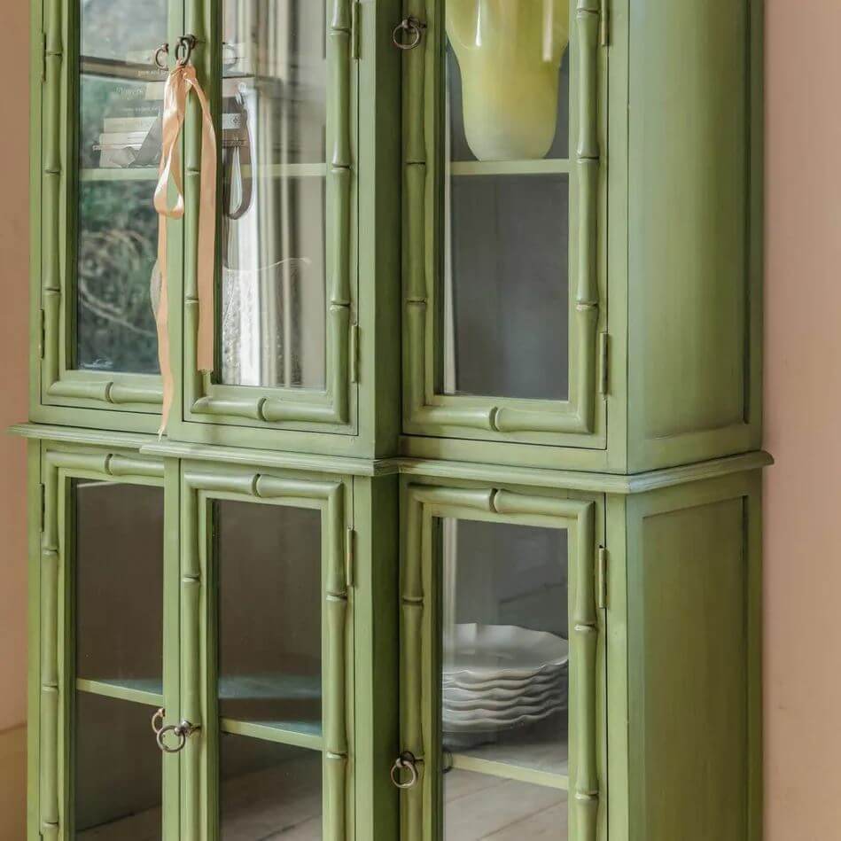 A tall, narrow green china cabinet with bamboo-style trim and glass doors.