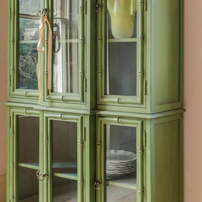 A tall, narrow green china cabinet with bamboo-style trim and glass doors.