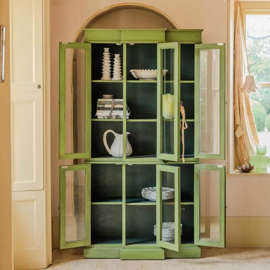 A tall sage green wooden cabinet with glass-paneled doors and open lower doors.