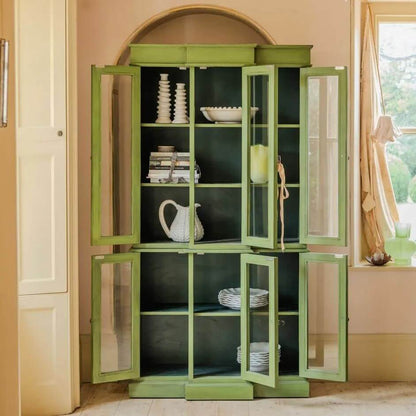 A tall sage green wooden cabinet with glass-paneled doors and open lower doors.