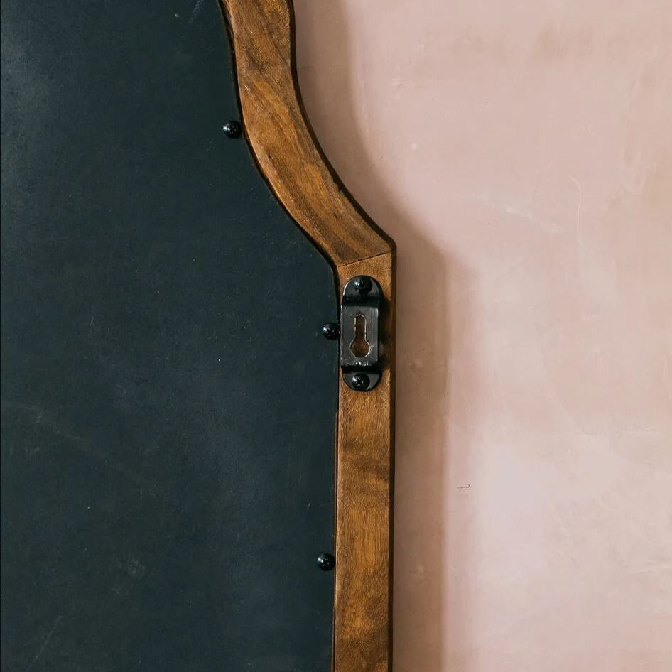 Close-up of a wall mirror showing a split design with a dark charcoal black reflective surface on the left and a warm medium-brown wooden frame on the right, featuring a vintage-style metal keyhole detail on the wood.
