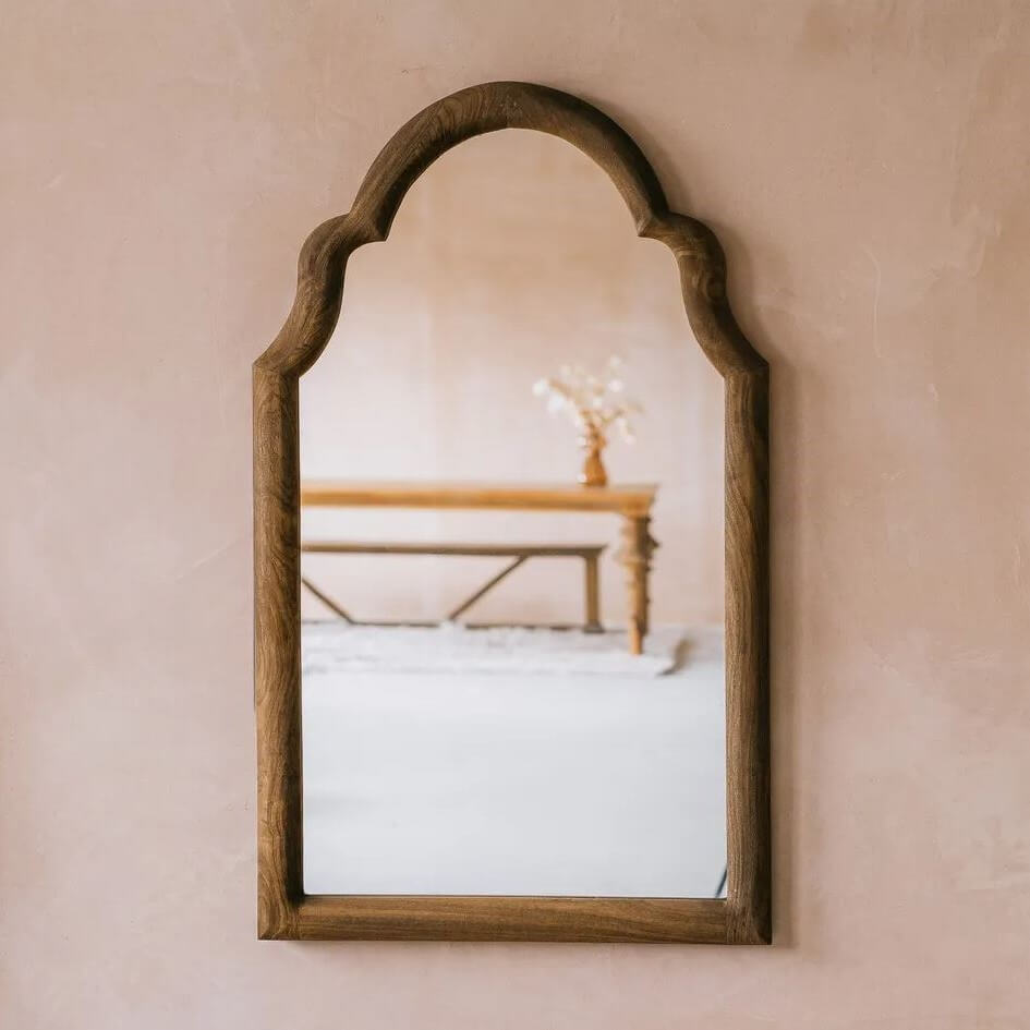 An arched wooden wall mirror with a dark brown frame.