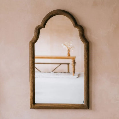 An arched wooden wall mirror with a dark brown frame.