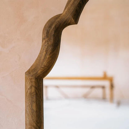 A close-up of a rustic, wavy wooden frame or mirror border with a rich dark brown wood grain.