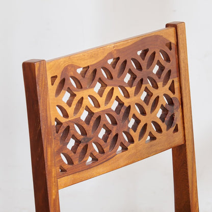 Close-up of a wooden chair back with an intricate geometric cutout pattern, showcasing warm medium-brown wood grain.