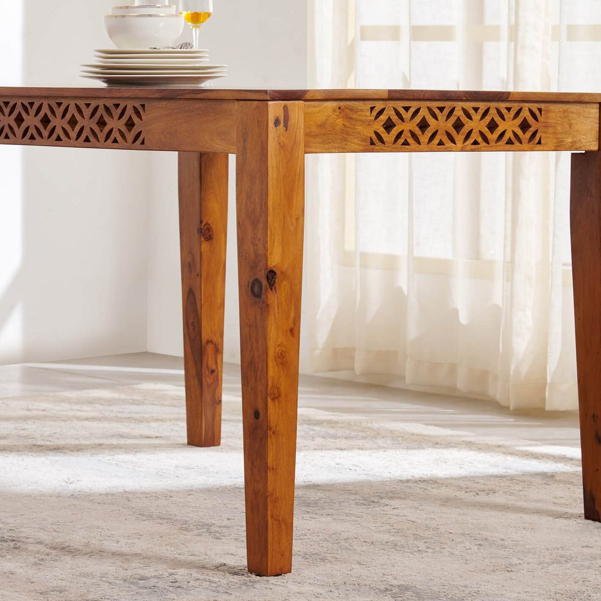 A warm medium-brown wooden dining table with carved geometric lattice details on the aprons.
