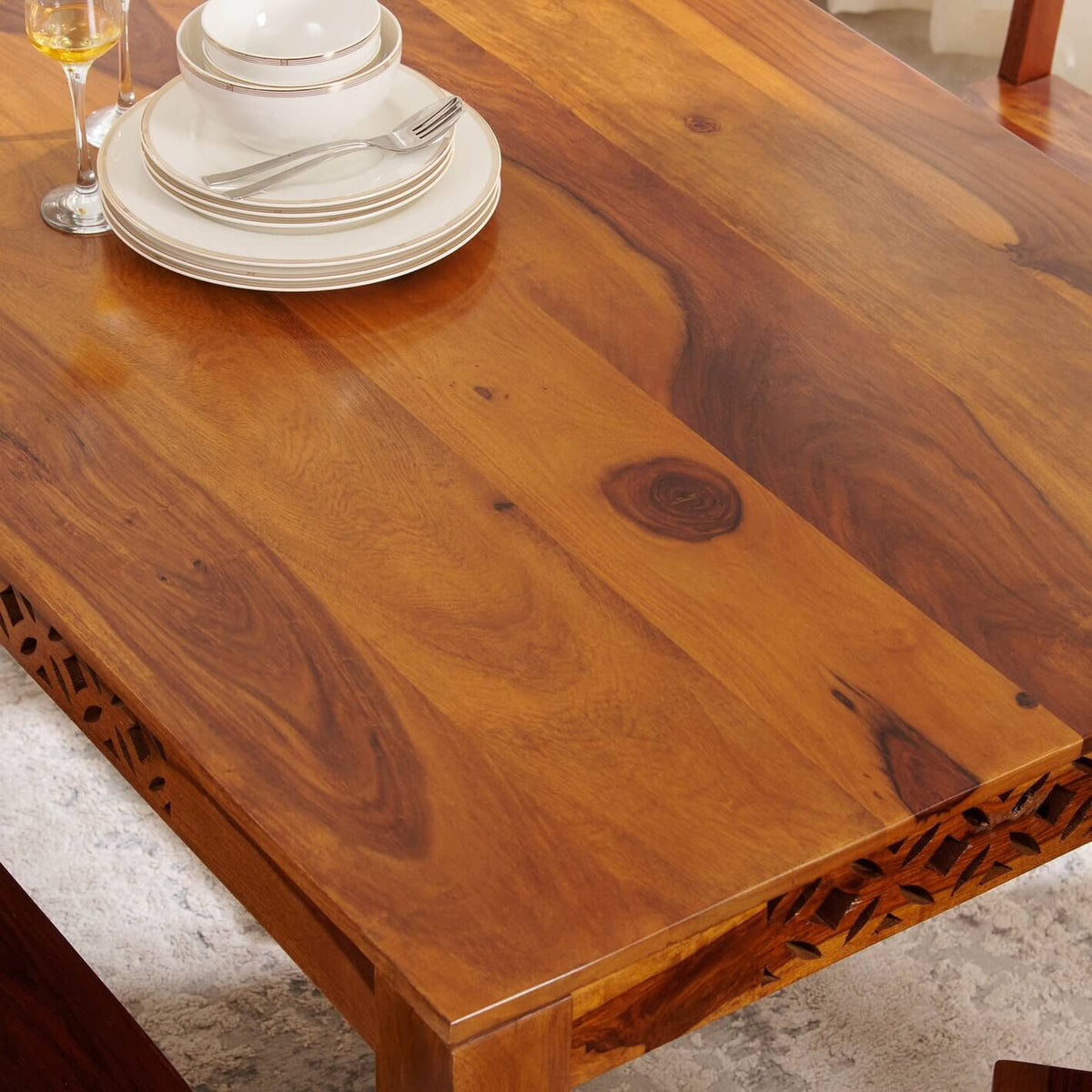 A close-up of a warm medium-brown wooden dining table with visible wood grain and carved details on the apron.