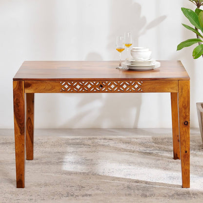 A rectangular wooden dining table with a carved geometric pattern on the apron.