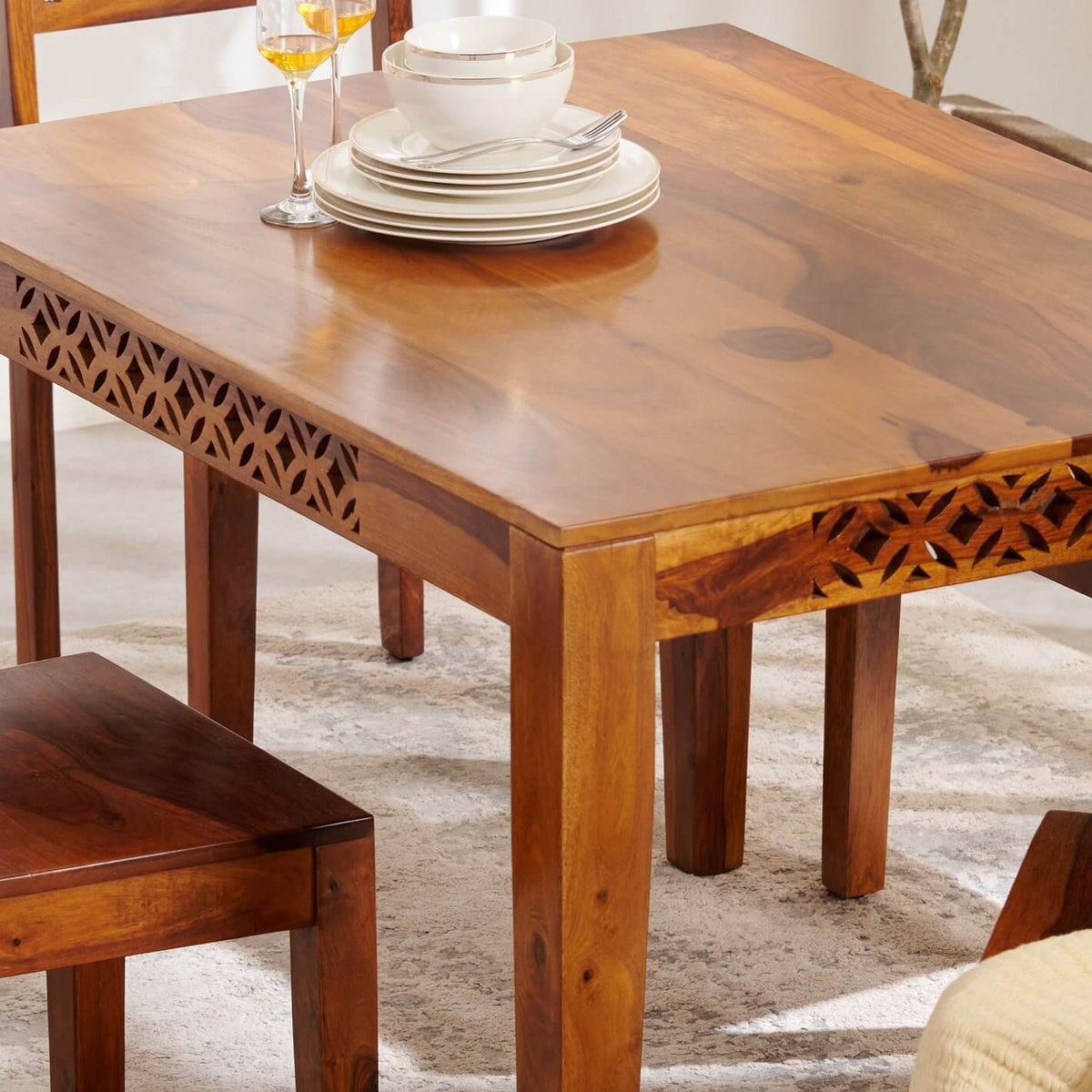 A rectangular wooden dining table with carved geometric details on the aprons.