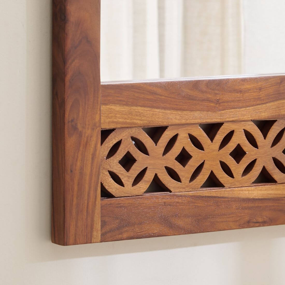 Close-up of a wooden wall mirror frame with a carved geometric lattice pattern and warm medium-brown wood grain.