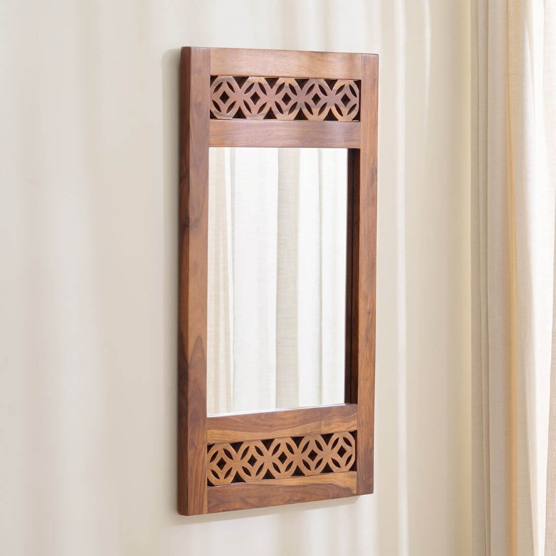 A vertical rectangular wooden wall mirror with decorative geometric cutout patterns at the top and bottom.
