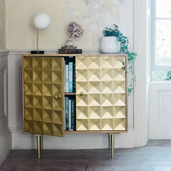 A gold-colored cabinet with a geometric pattern, featuring two doors and standing on metal legs.