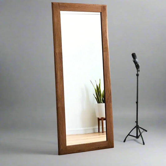 A full-length rectangular mirror with a wooden frame, reflecting a room.