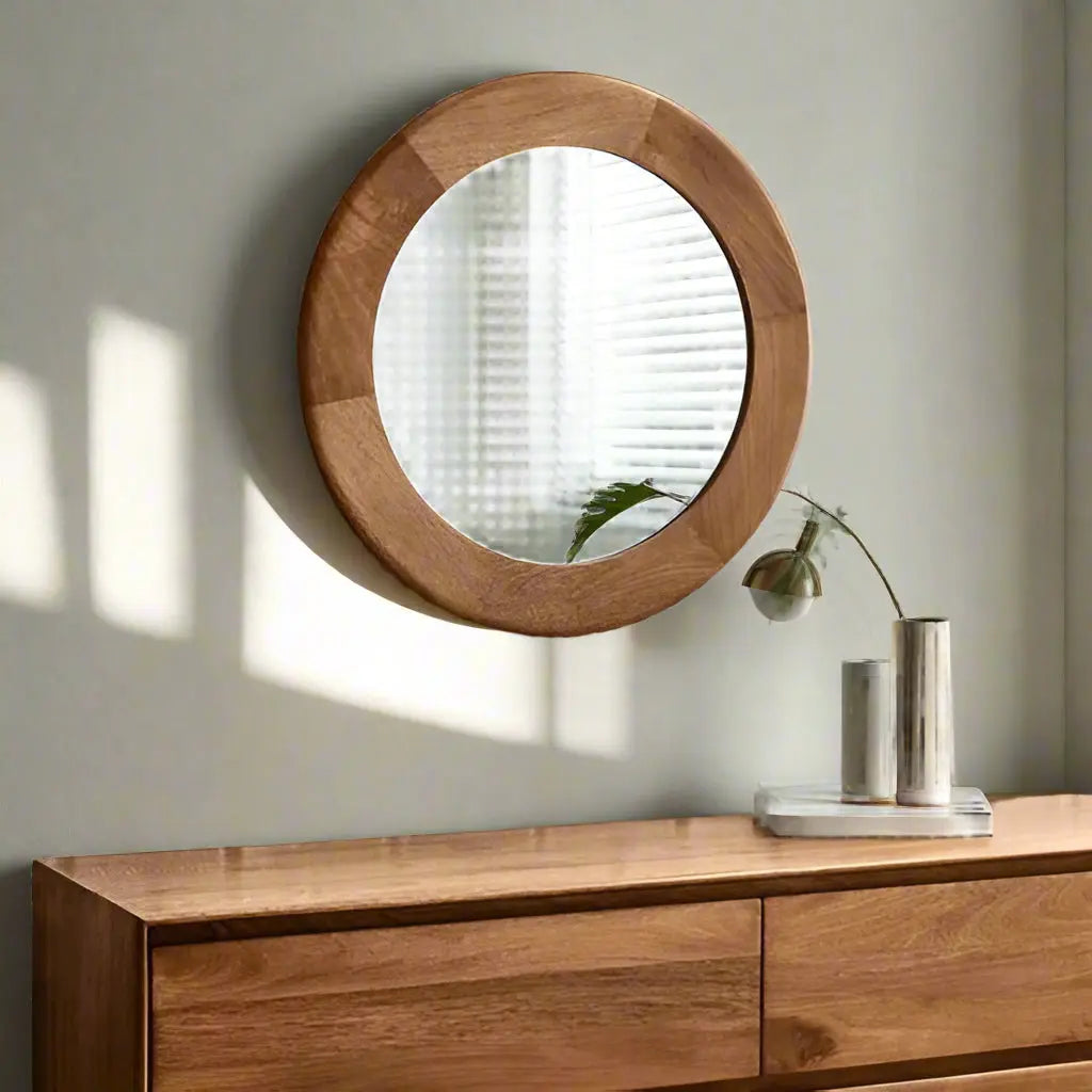 A round mirror with a wooden frame, hanging on a wall above a wooden dresser.