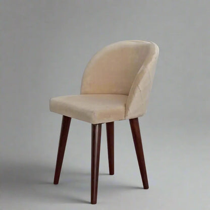 A beige upholstered chair with an upholstered backrest and seat, featuring knockdown sheesham wood legs, in a restaurant or dining room.