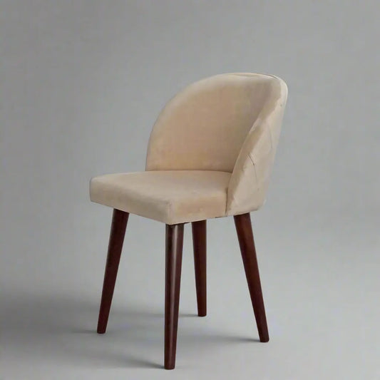 A beige upholstered chair with an upholstered backrest and seat, featuring knockdown sheesham wood legs, in a restaurant or dining room.