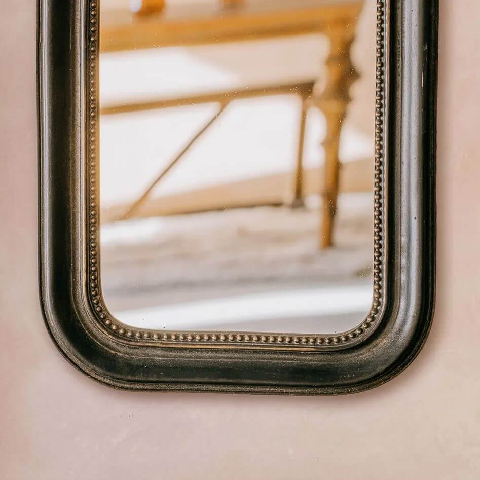 A close-up of an antique-style rectangular wall mirror with a dark finish   Metal beaded frame.