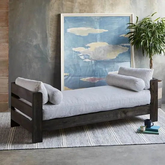 A black Raiden bed made of mango wood, displayed in a room setting with cushions on top.