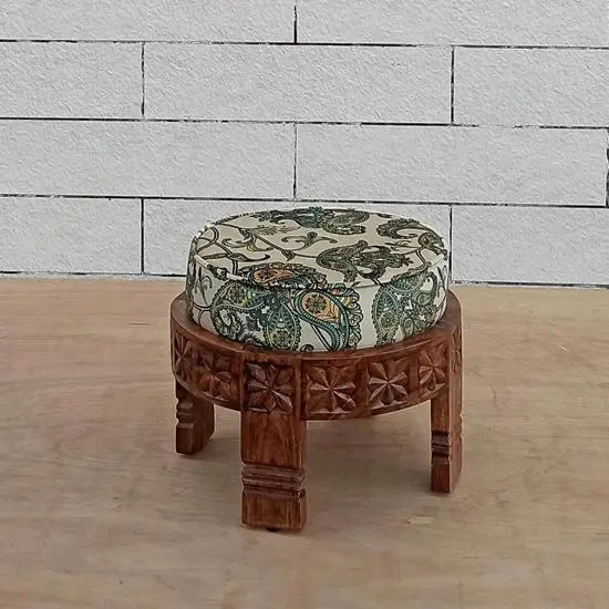 A hand-carved wooden footstool with a round shape and a printed velvet fabric.