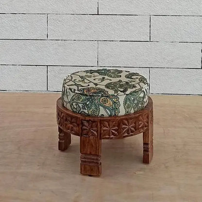 A hand-carved wooden footstool with a round shape and a printed velvet fabric.