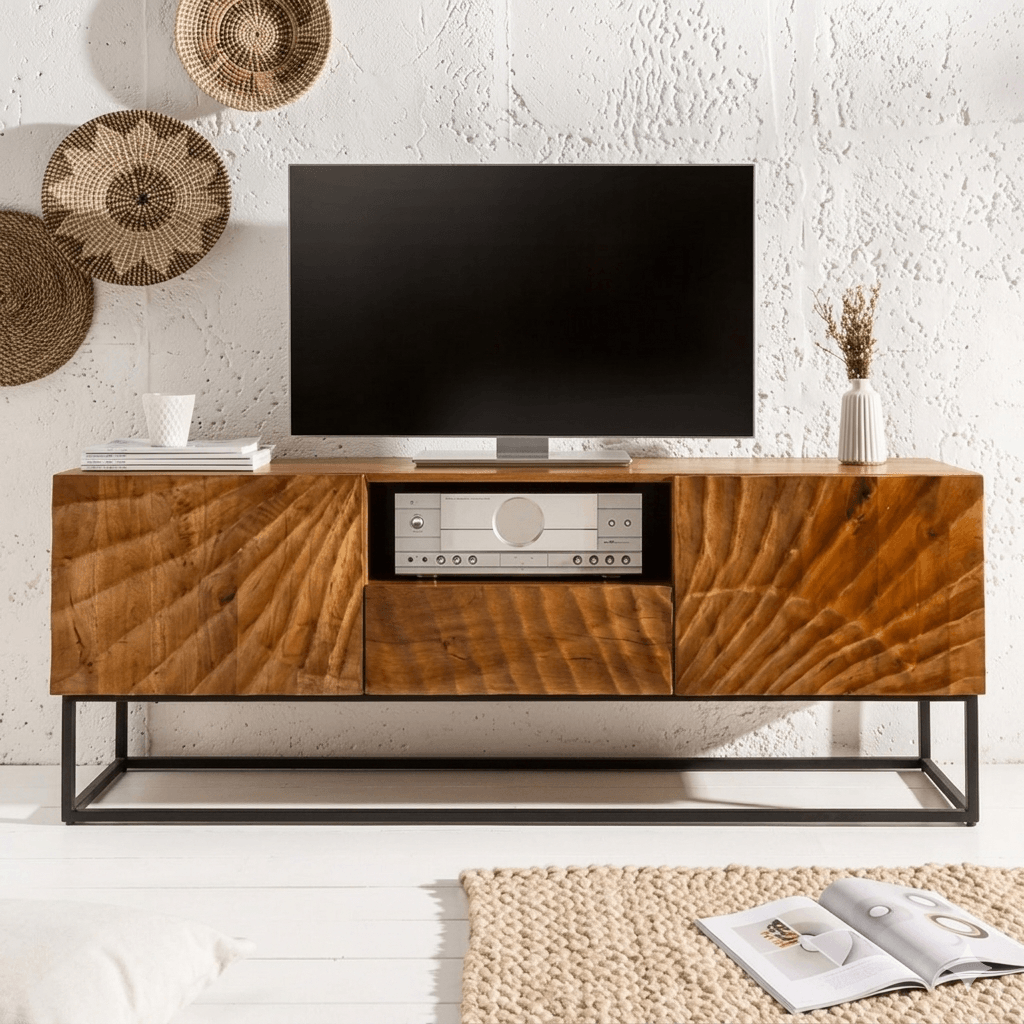 A stylish Wave TV cabinet made from high-quality mango wood with a warm honey tone finish, featuring two doors, one drawer, and an open shelf for storage. The cabinet has a sturdy metal base and is displayed in a living room setting with a flat-screen TV on top.