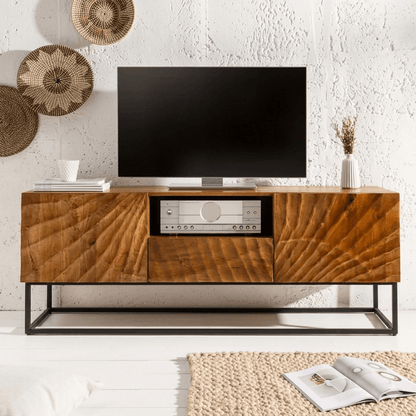 A stylish Wave TV cabinet made from high-quality mango wood with a warm honey tone finish, featuring two doors, one drawer, and an open shelf for storage. The cabinet has a sturdy metal base and is displayed in a living room setting with a flat-screen TV on top.