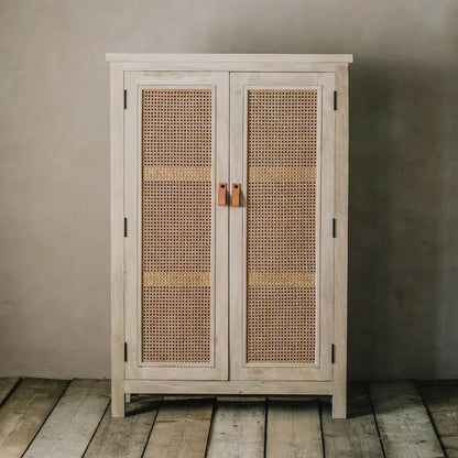 A rustic two-door cabinet with woven cane panels on the doors, finished in a light whitewashed wood tone with dark metal hinges and small wooden pull handles.