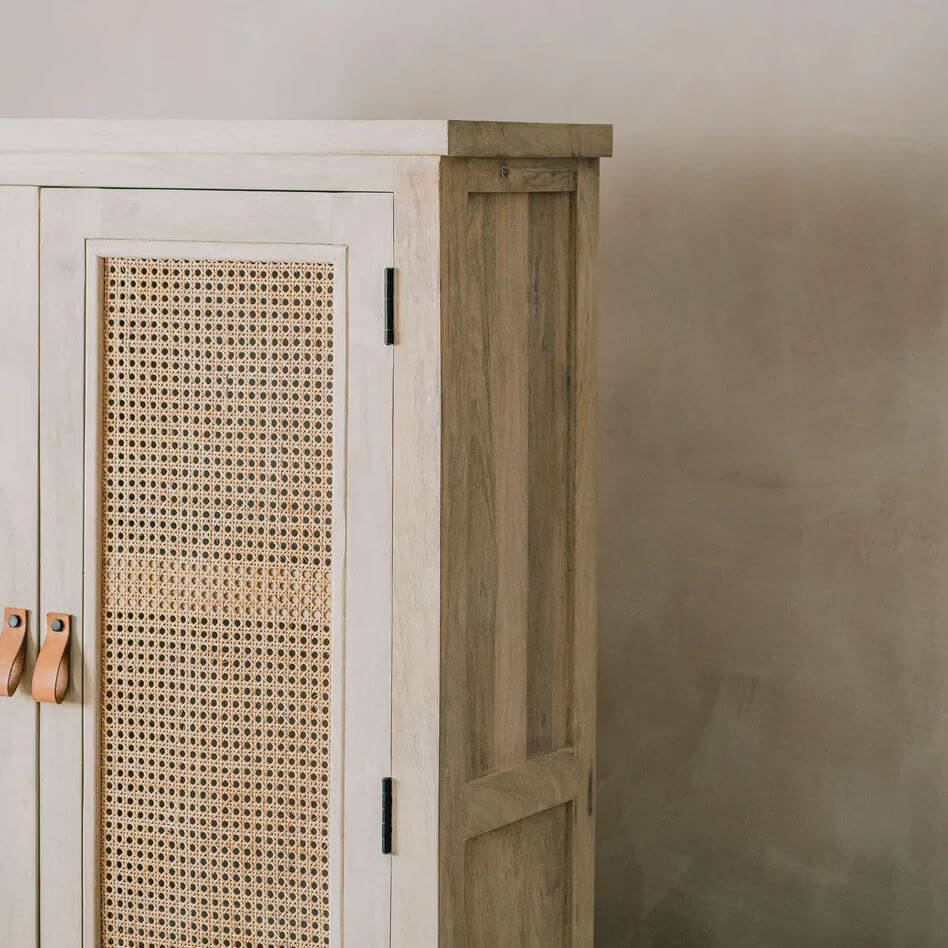 A close-up of a rustic wooden cabinet with a white-painted frame, natural cane paneling on the door, and light wood handles against a neutral.