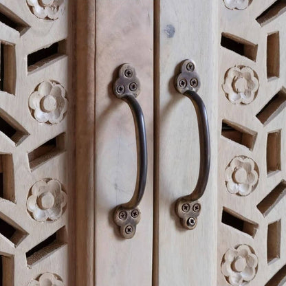Close-up of two dark metal cabinet handles mounted on a light natural wood door with carved geometric and floral patterns.